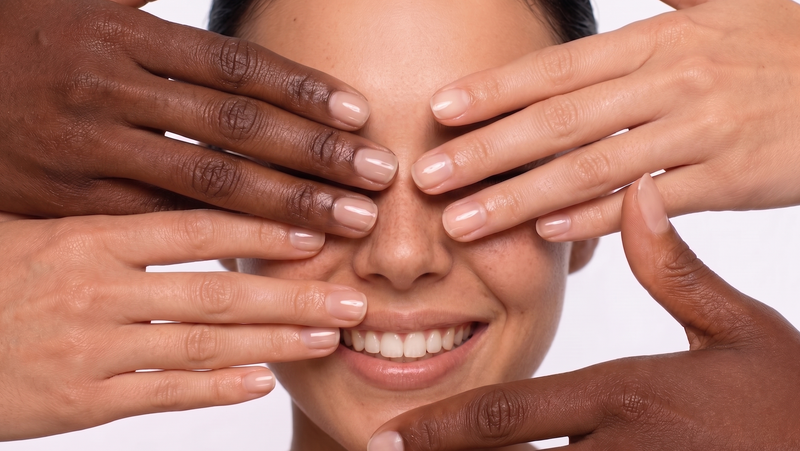 Smiling face framed by hands of different skin tones